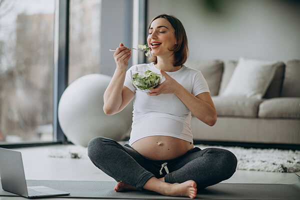 young pregnant woman eating salad at home, suggested by dietitian for pregnant women